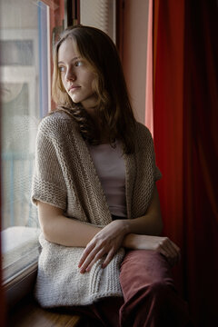 Young girl in cozy knitwear gazes thoughtfully out the window