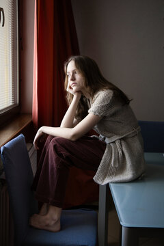 Young girl n in cozy knitwear gazes thoughtfully out the window