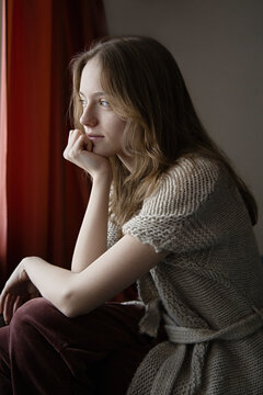 Young girl in cozy knitwear gazes thoughtfully out the window