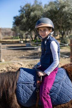 A young girl wearing a helmet and vest is riding a horse