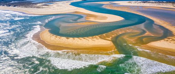 Naklejka premium Breathtaking Aerial View of a Winding River Delta Meeting the Turquoise Ocean with Golden Sandbanks, Intricate Water Channels, and Crashing White Surf in a Pristine Coastal Landscape Environment.