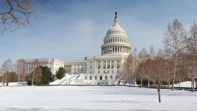 Famous Capitol building in Washington, D.C., covered in snow. The American flag flutters over the Capitol building in Washington, D.C. Clear, snowy day in the US capital.