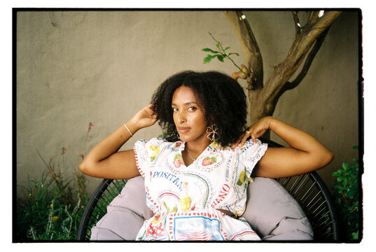 Portrait of a young woman sitting in her garden with her hands raised