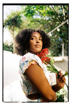 Mixed race woman holding red flowers in her garden
