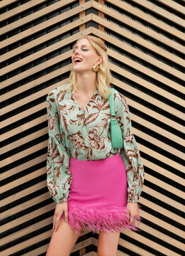 The girl in stylish summer outfit laughing in front of a wooden wall.
