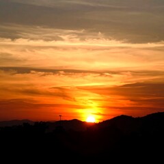 Obraz premium A vibrant sunset bathes the landscape in warm hues. The sun peeks behind distant mountains, casting long shadows across the horizon