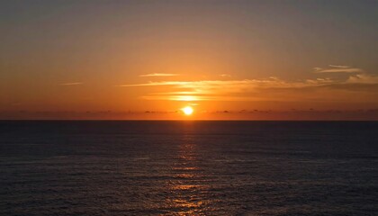 Obraz premium A vibrant sunset over the ocean. The sun is a bright orange orb reflected on the water's surface, with soft clouds