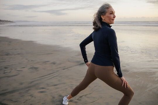 Mature Woman Stretching on Beach During Sunset in Activewear