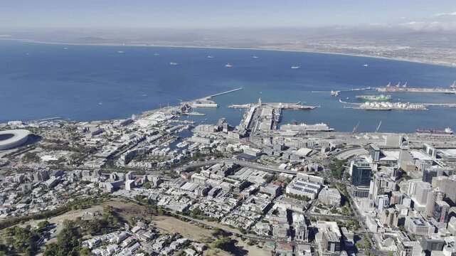 Drone flies backwards with view of V&A Waterfront and all the way to Big Bay across the water on a sunny morning in Cape Town, South Africa