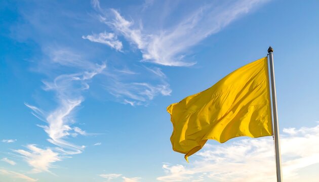 A vibrant yellow flag flutters gracefully on a pole, set against a backdrop of a bright blue sky with wispy clouds