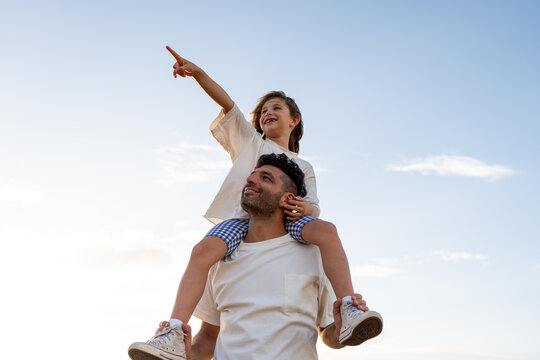 A dad lifts his daughter onto his shoulders, both laughing.