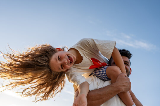 A dad lifts his daughter onto his shoulders, both laughing.