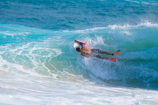 Full body photo of male bodyboarder suspended on face of tropical wave