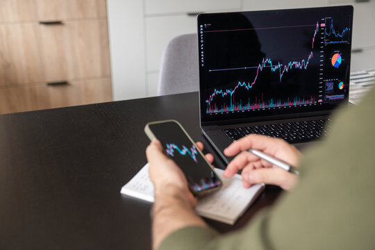 Person analyzing stock chart using phone and computer