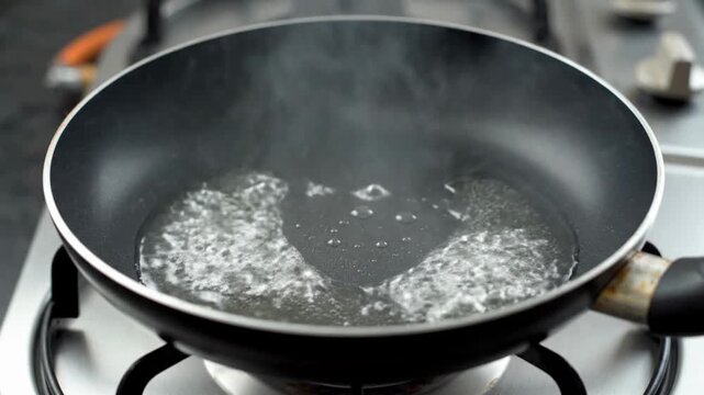 A close-up of boiling water in a pan, creating steam and bubbles.