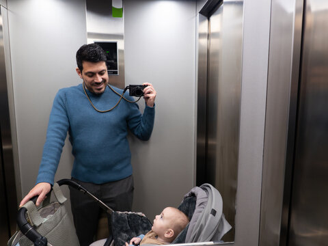 Father taking photos in elevator with baby in stroller