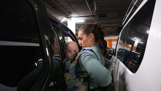Mother securing baby in carrier between cars in parking garage