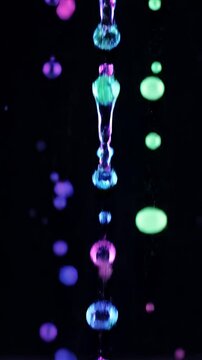 Colorful Liquid Droplets Falling Against A Dark Black Background With Blue Pink And Green Hues Creating A Mesmerizing