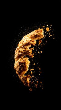 A dynamic, fragmented cookie piece scattering crumbs against a dark background, creating a vivid effect