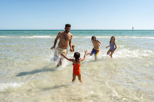 Kids running around in the water trying to catch dad.