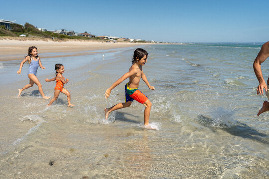 Kids running around in the water trying to catch dad.