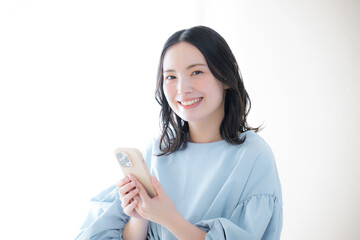スマホを操作する笑顔の女性 カメラ目線　オンライン利用・サービスなどの口コミや申し込みをするイメージ