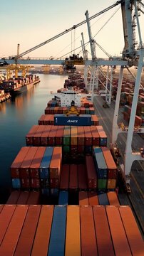 Massive Container Ship Docked at Bustling Industrial Port During Golden Hour Sunrise with Cranes Loading Cargo
