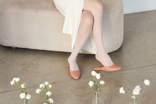 Elegant feet in white tights and stylish shoes resting on a cozy sofa
