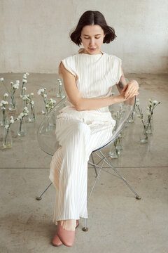 Woman in stylish white outfit sitting surrounded by flowers in vases