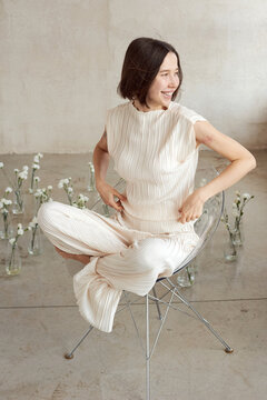 Stylish woman sitting in a clear chair surrounded by flowers 