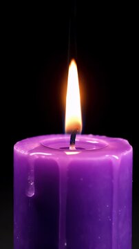 Close Up Of A Purple Hexagonal Pillar Candle Burning With Dripping Wax Against A Black Background With A Bright Orange