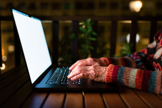 Senior hands typing on modern laptop at night