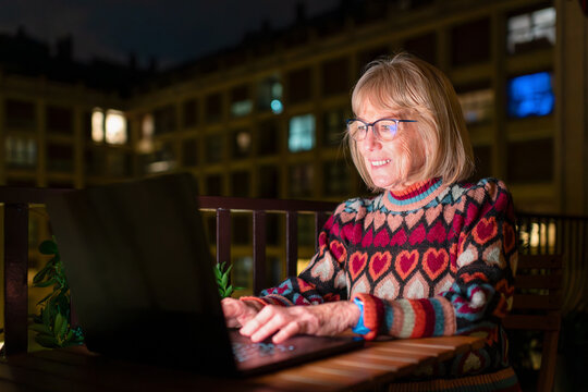 Senior woman using laptop on home terrace at night