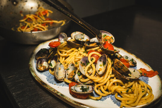 Clam being placed with tongs on pasta dish