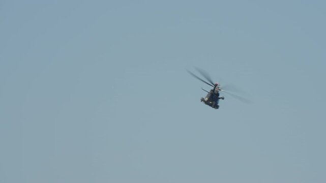 LUQA, MALTA - SEPTEMBER 28, 2025: A dark military helicopter banks and maneuvers against a vast, clear blue sky. A long shot shows the aircraft in flight, its rotors spinning, viewed from below.