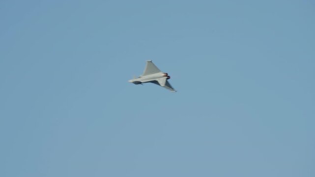 LUQA, MALTA - SEPTEMBER 28, 2025: A Eurofighter Typhoon fighter jet performs impressive aerobatic maneuvers against a clear blue sky. The military aircraft banks, rolls, and turns, showcasing its