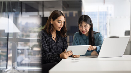 Serious diverse female managers analyzing online content on tablet together, pointing at screen,...
