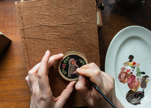 Artist painting a delicate bird on a wooden slice