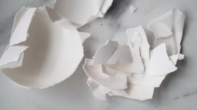 Close up of shattered white eggshells on a speckled marble surface, abstract background