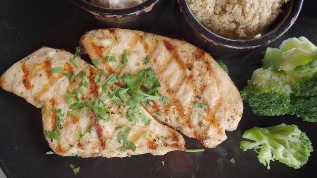 Grilled chicken breast with fresh broccoli and couscous on black plate close up motion video clip
