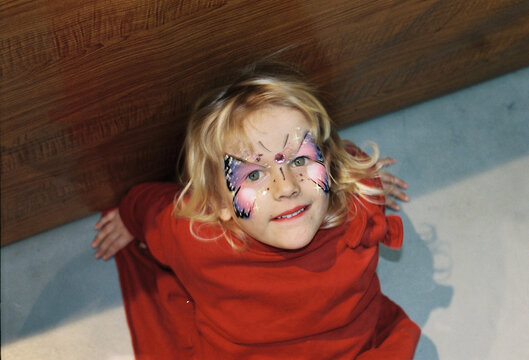 Young girl with butterfly face painting poses happily 