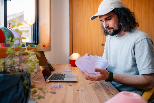 A person inspecting lamp shade at desk with laptop