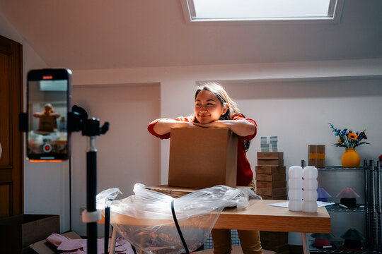 Smiling woman leaning on branded box during video shoot at home