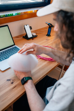 Man assembles lamp part at wooden desk with laptop