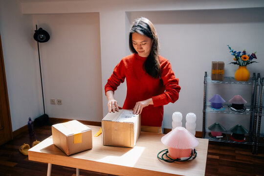 Woman prepares delivery parcel in sunny workspace