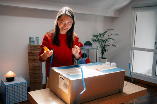 Woman smiles while preparing package with cutter