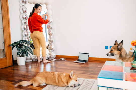 Woman decorating sculptural mirror near dogs and laptop