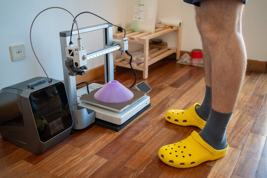 Man using 3D printer to print purple object at home