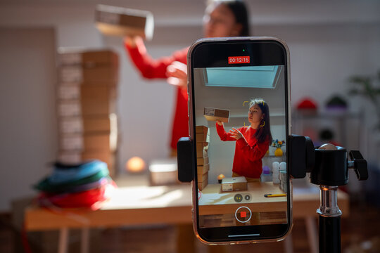 Filming woman packing boxes for business with smartphone