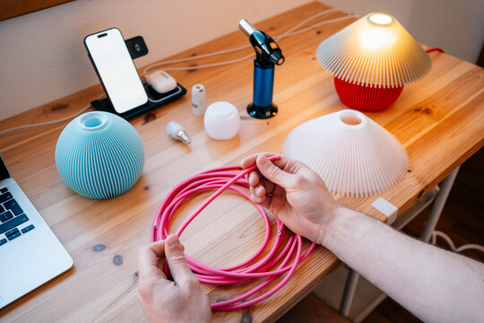 Hands holding pink cable at colorful lamp-making workspace